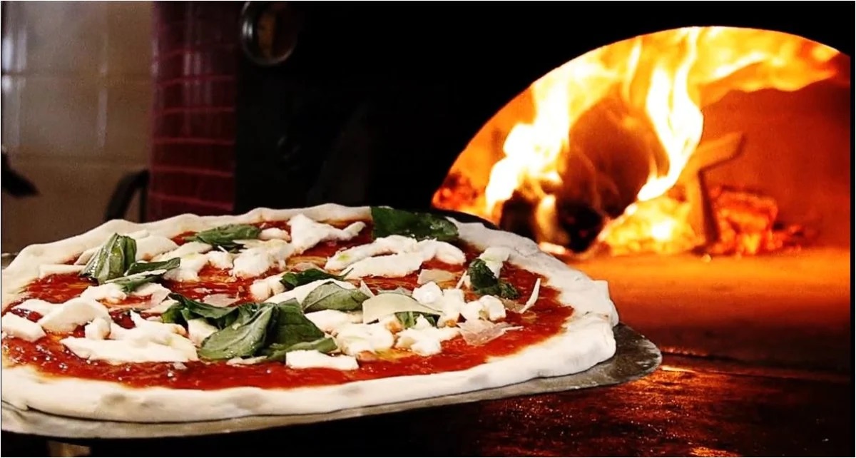 Margherita pizza coming out of the wood-fired brick oven