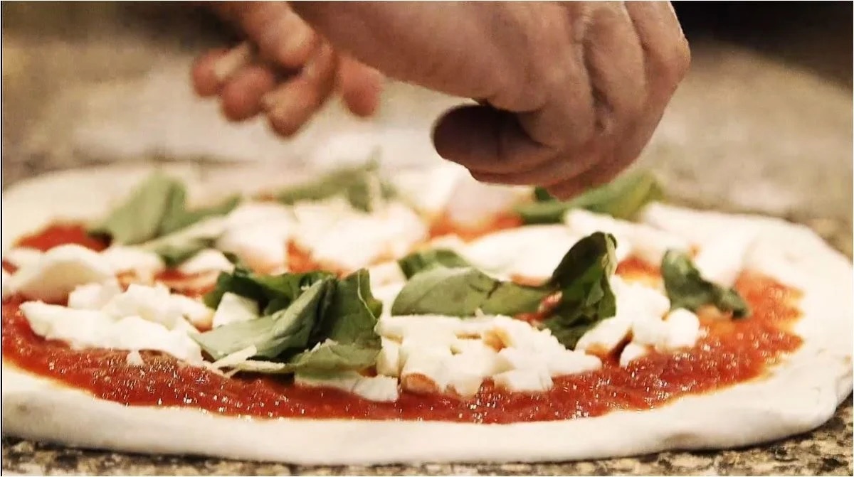 Fresh mozzarella and basil being added to pizza dough